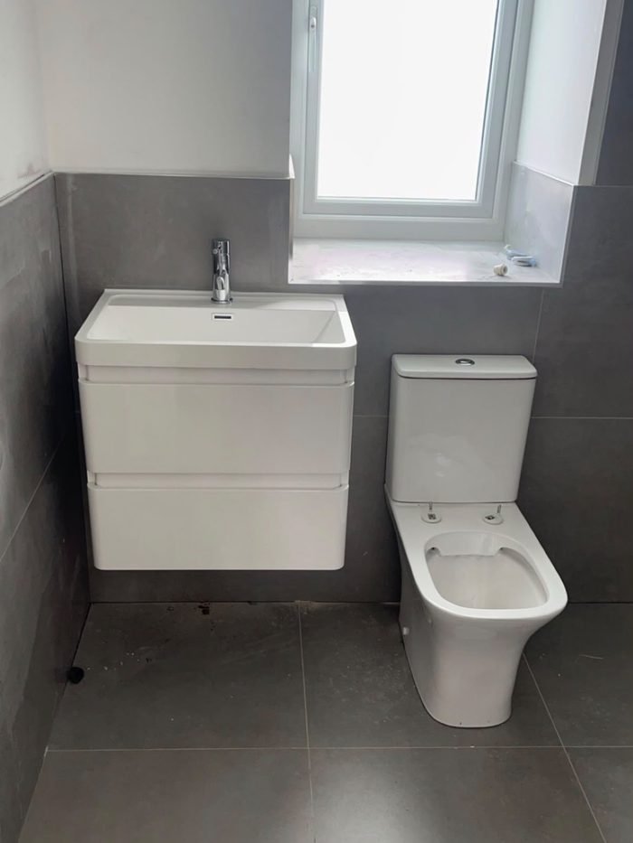 A completed bathroom with a wall-hung vanity unit, basin and close-coupled WC against large grey tiles