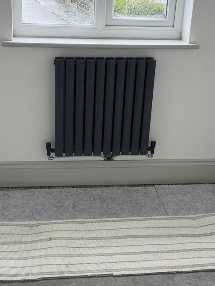 A black anthracite designer column radiator fitted beneath a window in a newly decorated room